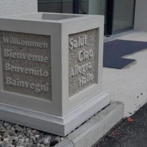 Quadratischer Blumentopf aus Beton mit eingearbeiteten Willkommen-Grüssen in mehreren Sprachen